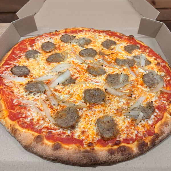 A whole pizza with sausage and onions in a cardboard delivery box.