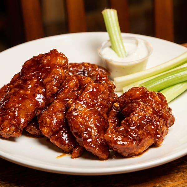 Plate of saucy chicken wings, celery sticks, and a creamy dip on a rustic wooden table.