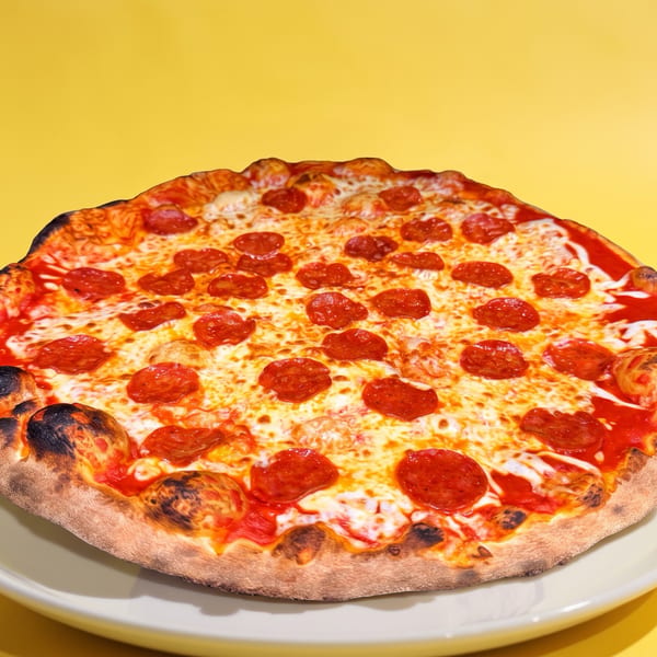 A whole pepperoni pizza with a crispy crust and melted cheese on a white plate against a yellow background.