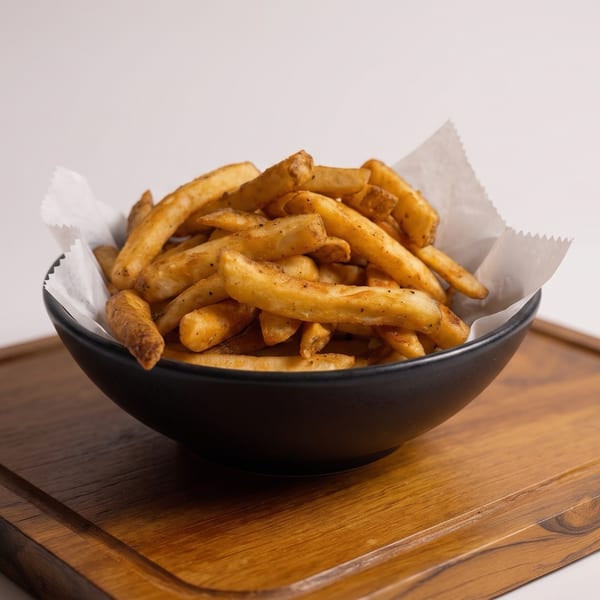 Golden seasoned fries piled in a black paper-lined bowl on a wooden serving board.