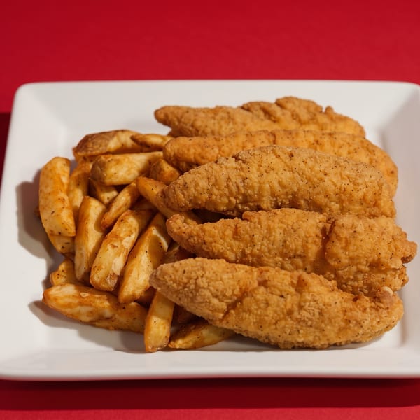 Crispy chicken tenders and seasoned potato wedges on a white rectangular plate against a red background.