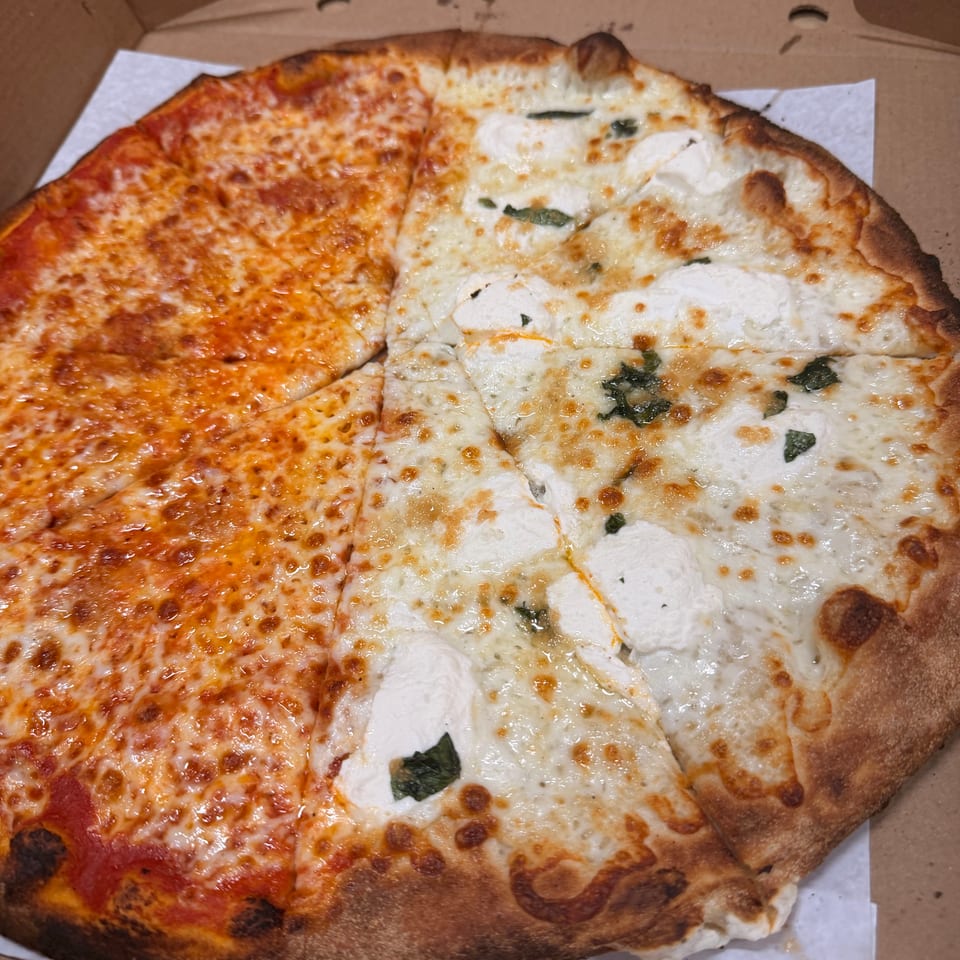Large half-and-half cheese pizza in a cardboard box, with tomato sauce on one side and fresh mozzarella and basil on the other.
