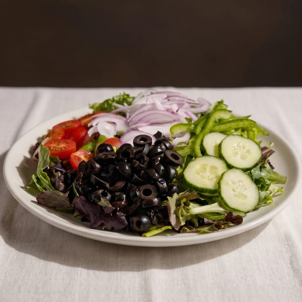 A fresh garden salad with lettuce, tomatoes, red onions, green peppers, cucumbers, and black olives.