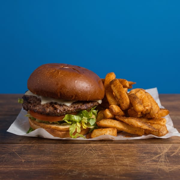 Juicy cheeseburger with lettuce and tomato served alongside seasoned golden fries on a paper-lined wooden table.