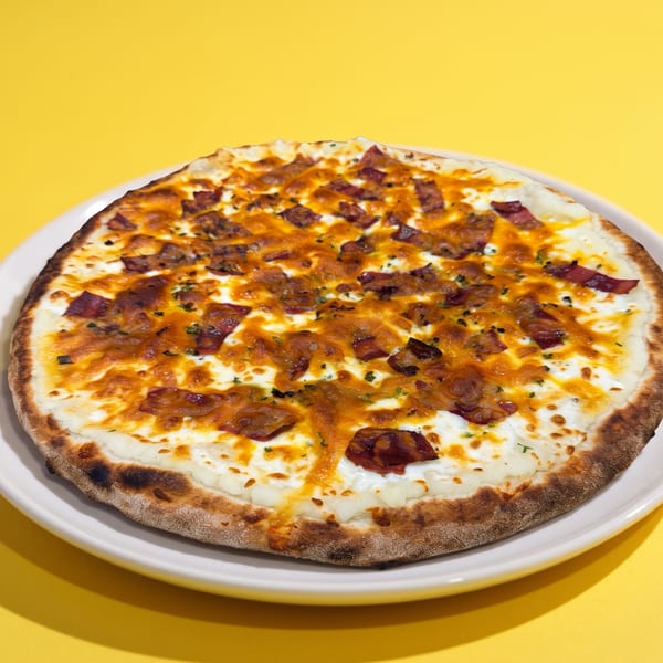 A golden-crusted pizza with white sauce, melted cheese, and bacon bits on a white plate.