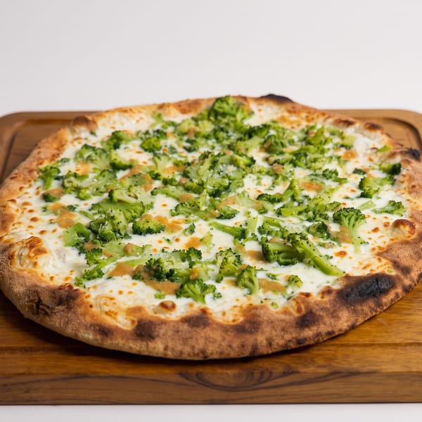 Cheesy broccoli pizza with a charred crust sits on a wooden serving board.