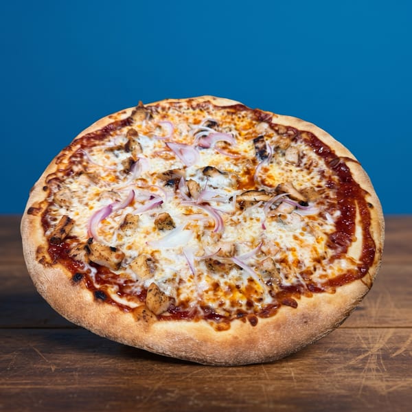 A whole BBQ chicken pizza with red onions and melted cheese on a wooden table.