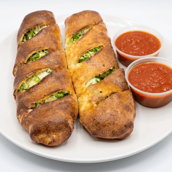 Two golden-brown strombolis filled with broccoli and cheese, served with two cups of marinara sauce.