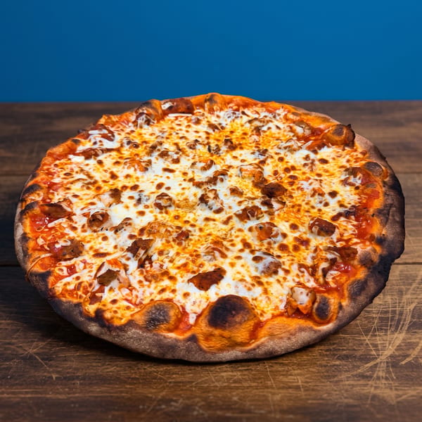 Large cheese pizza topped with sausage pieces and tomato sauce, resting on a rustic wooden table against a blue background.