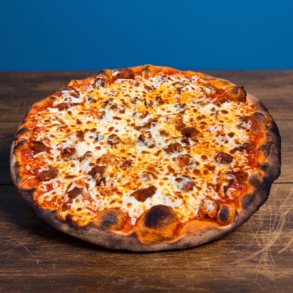 Large cheese pizza topped with sausage pieces and tomato sauce, resting on a rustic wooden table against a blue background.