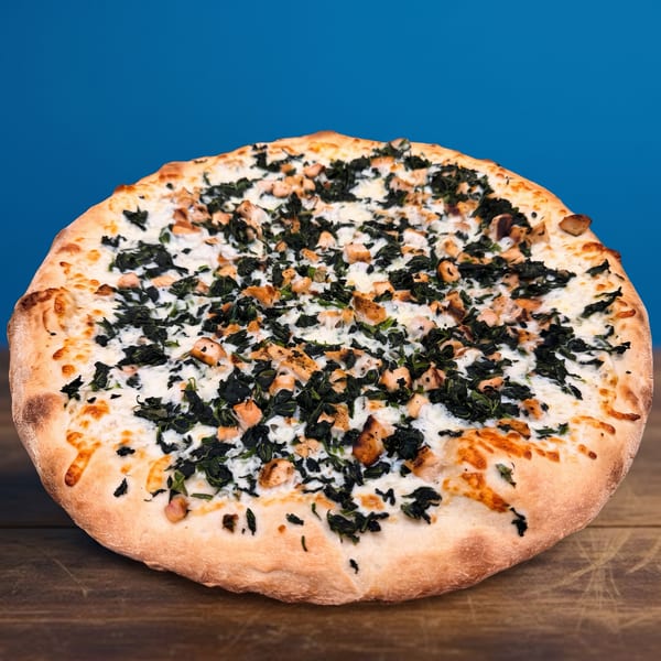 A whole white pizza with spinach and chicken pieces on a wooden table.