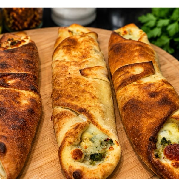Three golden-brown strombolis with visible cheese and broccoli fillings, served with marinara sauce.