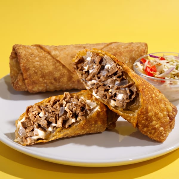 Crispy meat-filled pastries sit on a white plate with shredded vegetable salad against a bright yellow background.