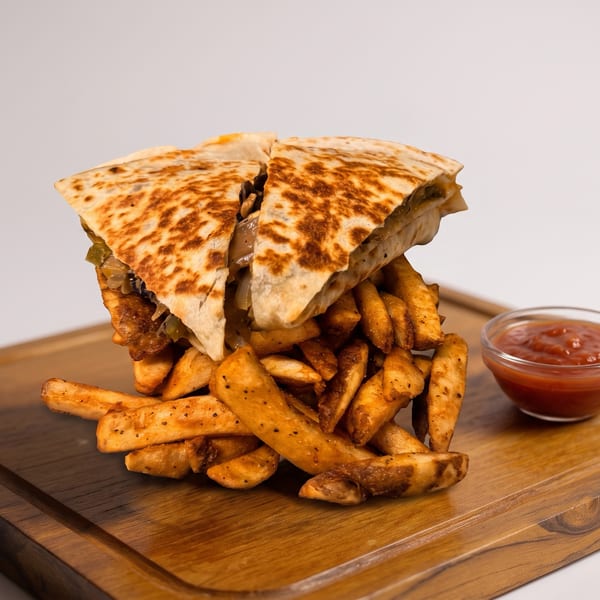 Grilled quesadilla wedges stacked over seasoned fries on a wooden serving board, with a bowl of red dipping sauce.