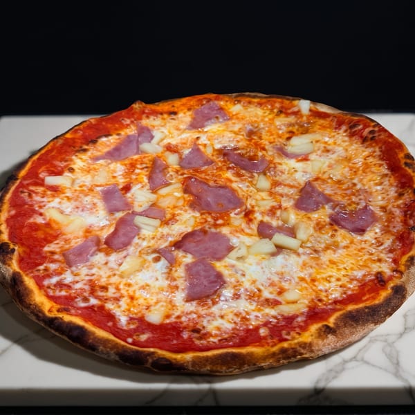A Hawaiian pizza with ham and pineapple on a white marble slab.